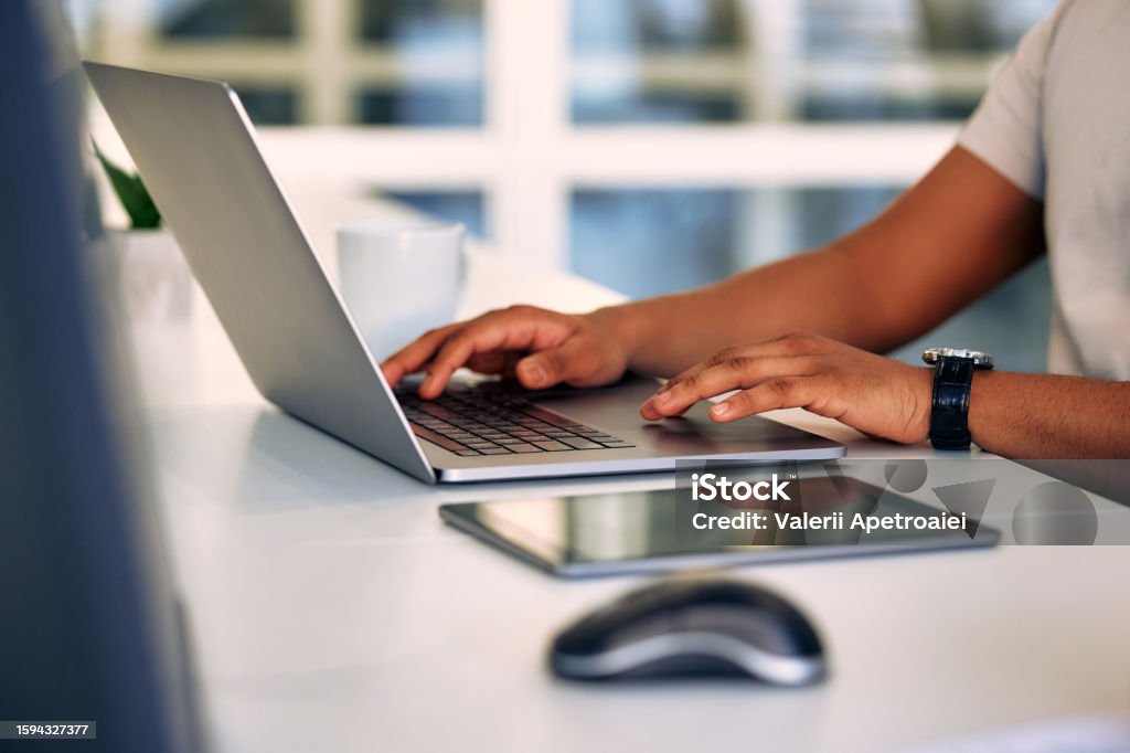 Cropped image of a man, freelancer, businessman, or call center worker working while sitting at a laptop at a desk in an office or coworking space. Remote work from home.